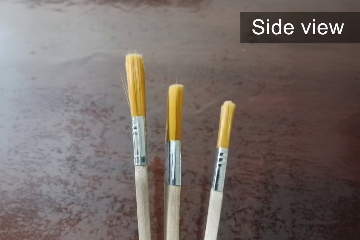 Three paintbrushes with yellow bristles on a marbled surface