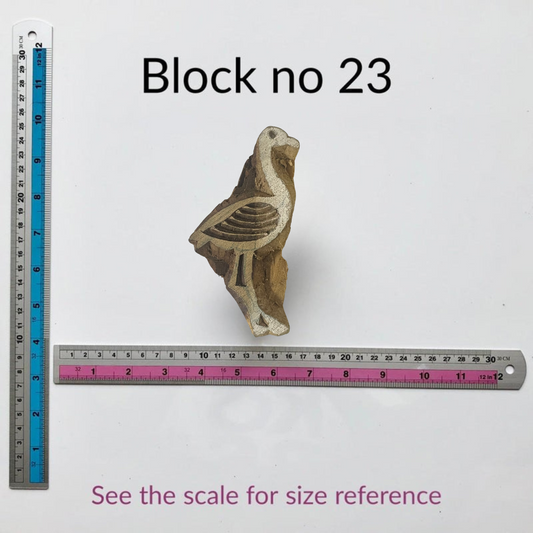 Small wooden block with bird design next to a ruler for size reference on a white background